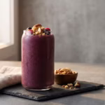 Copo com smoothie proteico de açaí decorado com castanhas do pará sobre superfície escura representando nutrição de alta performance